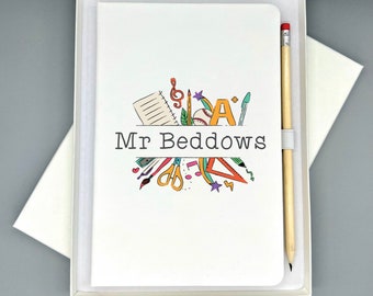 May include: A white notebook with a colourful illustration of school supplies, including a pencil, ruler, scissors, and a notebook. The text "Mr. Beddows" is printed on the notebook. The notebook is in a white box with a pencil.
