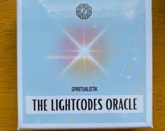 May include: A white box with a blue background and a white starburst design. The box has the text "SPIRITUALISTIK THE LIGHTCODES ORACLE" printed on it.