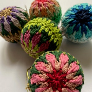 May include: Five crocheted Christmas ornaments in various colors and patterns. The ornaments are green, pink, red, blue, and purple. They are all round and have a textured surface.