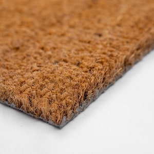 May include: Close-up of a brown coir doormat with a black backing. The mat is made of natural fibers and is designed to help trap dirt and moisture.