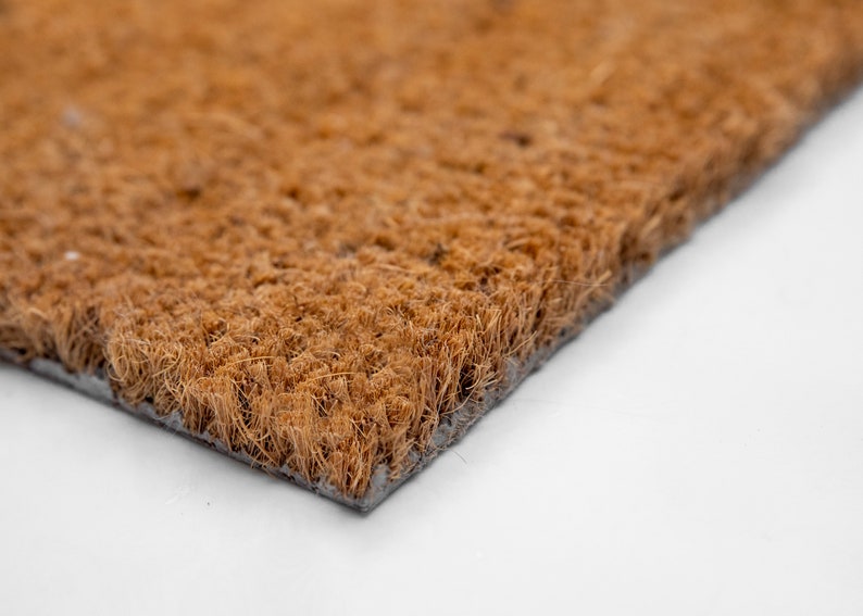 May include: Close-up of a brown coir doormat with a black backing. The mat is made of natural fibers and is designed to help trap dirt and moisture.
