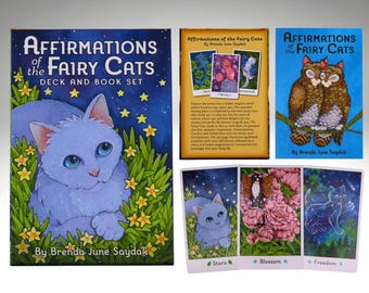 May include: A deck and book set titled "Affirmations of the Fairy Cats" featuring a blue cat illustration. The set includes a book, cards with illustrations of cats, flowers, and stars, and the text "Stars", "Blossom", and "Freedom".