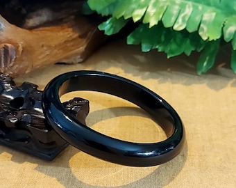 May include: A black bangle bracelet made of polished jade. The bracelet is smooth and shiny, and it has a simple, elegant design.
