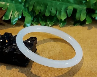 May include: A white jade bangle bracelet. The bracelet is smooth and polished, and it has a simple, elegant design.