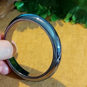 May include: A black, shiny, smooth bangle bracelet. The bracelet is made of a hard, durable material and has a simple, elegant design.