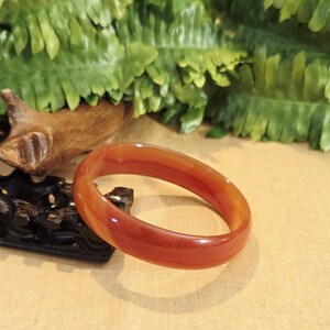 May include: A red agate bangle bracelet. The bracelet is smooth and polished, with a slight orange hue.