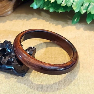 Puede incluir: Un brazalete de madera marrón oscuro con un acabado liso y pulido.