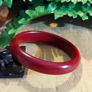 Puede incluir: Un brazalete redondo de madera pulida de color rojo oscuro. El brazalete tiene una superficie lisa.