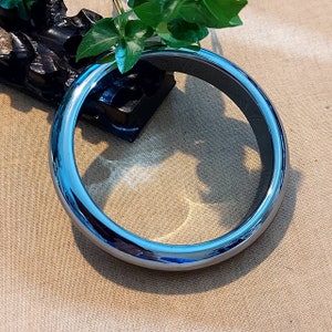 May include: A shiny, silver-coloured bangle bracelet with a smooth, rounded surface.