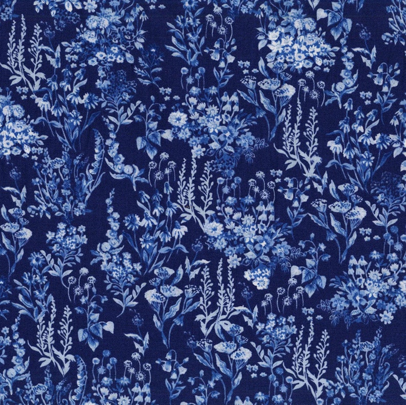 Op de afbeelding: Een donkerblauwe stof met een dicht, herhalend patroon van witte en lichtblauwe wilde bloemen, inclusief diverse stengels, bladeren en bloesems die in een botanische illustratiestijl over het gehele oppervlak van het textiel zijn gerangschikt.
