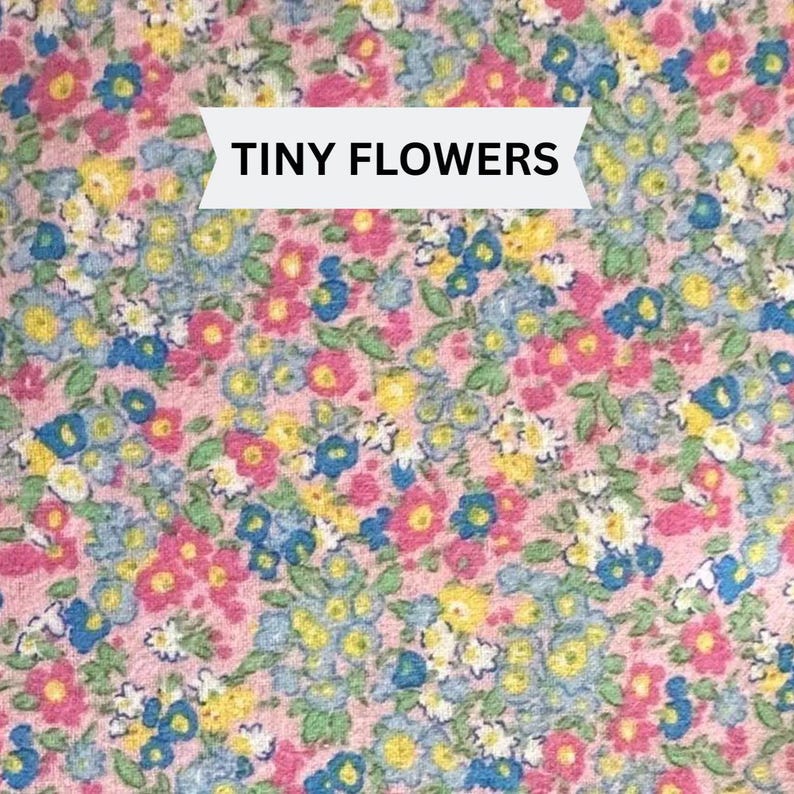 Pu&ograve; includere: Un motivo in tessuto caratterizzato da una fitta disposizione di minuscoli fiori nelle tonalit&agrave; del rosa, blu, giallo e bianco su uno sfondo rosa tenue. Un banner bianco sovrapposto al centro mostra il testo nero TINY FLOWERS.