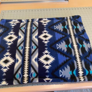 May include: A square fleece mat featuring a geometric pattern in shades of navy blue, royal blue, light blue, black, white, and gray. The fabric has a soft texture and is displayed on a cutting mat with visible inch markings along the edges.