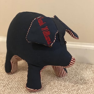 May include: A blue and red striped fabric pig with a red embroidered name "Frank Williams" on the side.