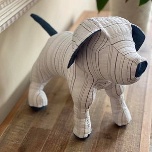 Könnte beinhalten: Ein gestreiftes Stoffspielzeug für Hunde in Weiß und Blau. Der Hund steht auf einer Holzoberfläche.