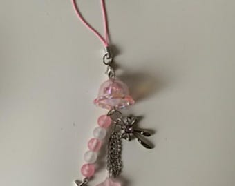 May include: A pink and white charm with a pink cord. The charm features a clear, bell-shaped top, pink and white beads, a star, a cross, and a flower charm. The charm is attached to a silver chain.