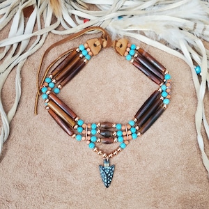 May include: A multi-strand necklace with brown wooden beads, turquoise beads, and copper beads. The necklace has a copper arrowhead pendant.