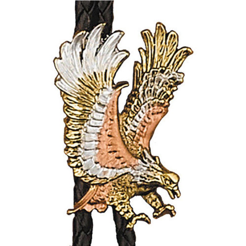 May include: A gold, silver and copper bolo tie featuring a detailed eagle design with wings spread. The eagle is perched on a black leather cord.