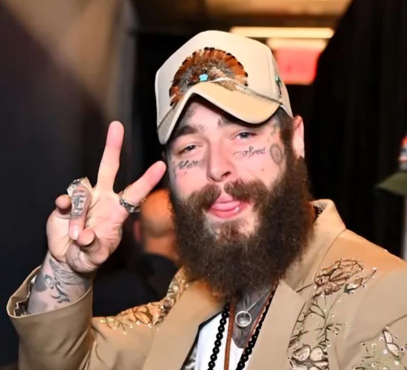 Puede incluir: Gorra de b&eacute;isbol beige con plumas y detalles turquesas. La persona lleva una blazer beige con bordados florales. La persona tiene tatuajes faciales y una larga barba. La persona hace el signo de la paz.