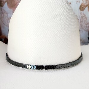 Pu&ograve; includere: Un cappello da cowboy bianco con una fascia nera a forma di freccia.