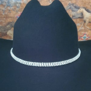 Peut inclure: Un chapeau de cowboy noir avec une bande de strass argentée autour de la couronne.