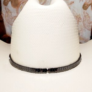 Pu&ograve; includere: Un cappello da cowboy bianco con una fascia nera a forma di chevron.