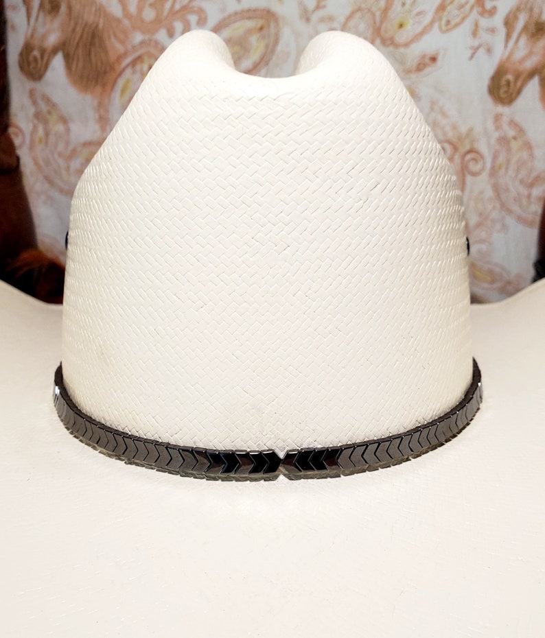Pu&ograve; includere: Un cappello da cowboy bianco con una fascia nera a forma di chevron.
