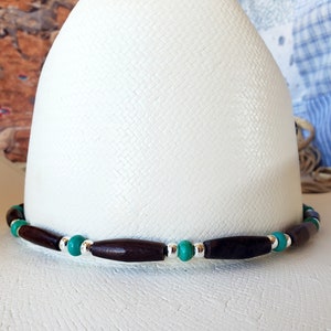 May include: A white cowboy hat with a brown and silver beaded hat band. The beads are turquoise and silver.