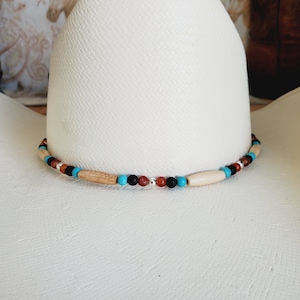 May include: A white cowboy hat with a beaded hat band. The hat band is made of turquoise, brown, black, and white beads.