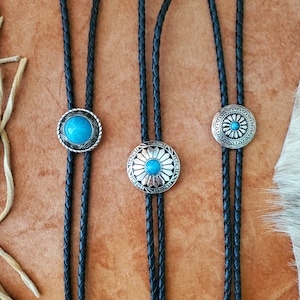 May include: Three black bolo ties with silver and turquoise bolo tips. The bolo tips feature a floral design.