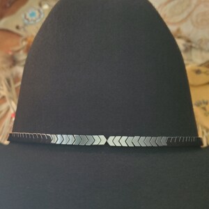 Pu&ograve; includere: Un cappello da cowboy in feltro nero con un bordo di punte di freccia argentate e nere attorno alla corona.