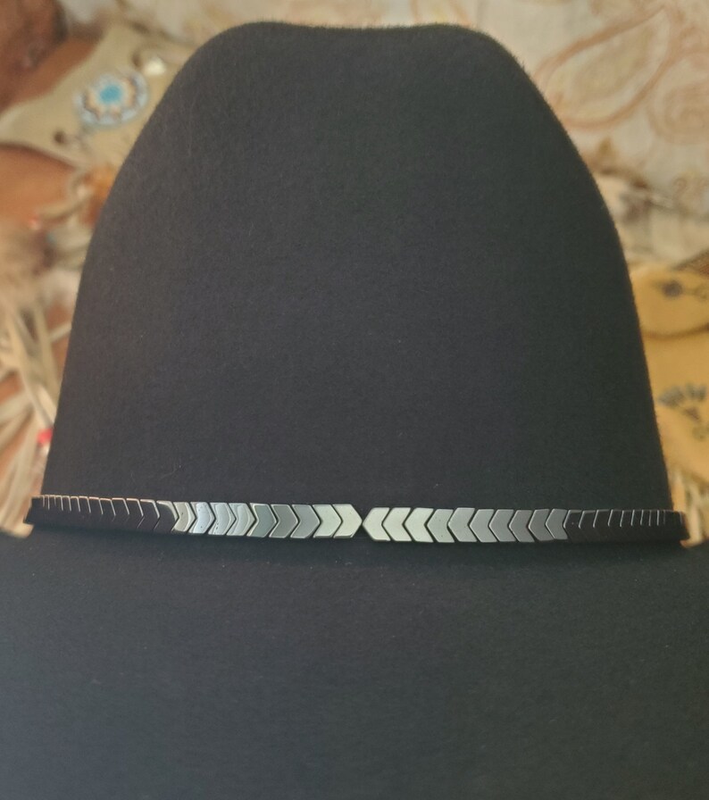 Pu&ograve; includere: Un cappello da cowboy in feltro nero con un bordo di punte di freccia argentate e nere attorno alla corona.