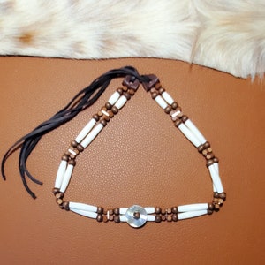 May include: A white and brown beaded necklace with a white circular pendant. The necklace has a leather cord with a tassel.