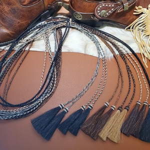 May include: A set of eight braided leather boot laces with tassels. The laces are in various colors, including black, brown, and white. The tassels are made of horsehair and are in black, brown, and tan.