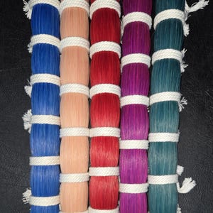 May include: A close-up shot of five vertical columns of colorful, cylindrical objects. Each column is a different color: blue, peach, red, purple, and teal. Each cylinder is wrapped with white rope at intervals, creating a textured pattern.