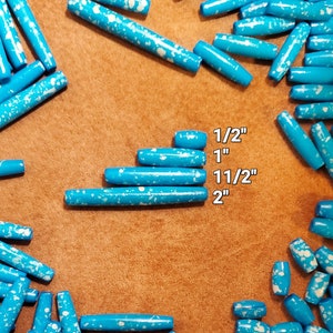 Op de afbeelding: Een verzameling turquoise blauwe houten kralen met witte verfspatten. De kralen zijn in verschillende maten, variërend van 1,27 cm tot 5,08 cm. De kralen zijn in een cirkel op een bruin oppervlak gerangschikt.
