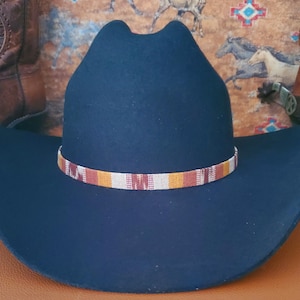 Puede incluir: Un sombrero de vaquero negro con una banda de color marrón, naranja y blanco.
