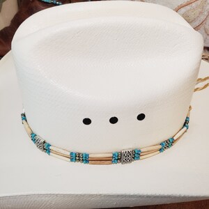 May include: White cowboy hat with a turquoise and bone bead hat band with silver accents.