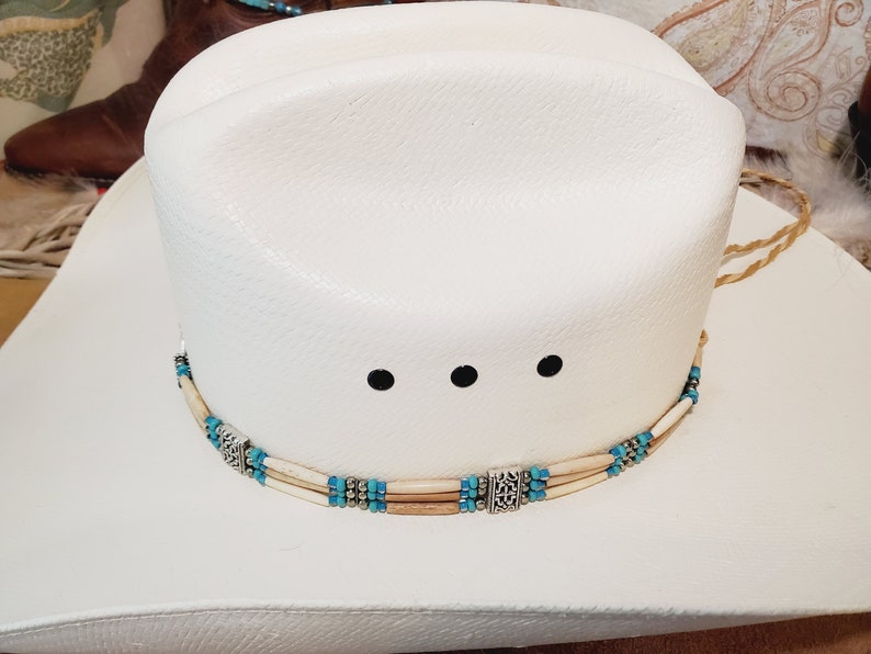 May include: White cowboy hat with a turquoise and bone bead hat band with silver accents.