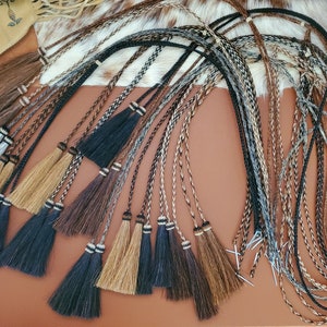 May include: A collection of braided leather cords with tassels, featuring a variety of colors and patterns, including black, brown, tan, and gray.