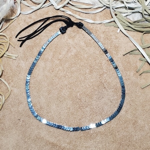 Pu&ograve; includere: Una collana d'argento con una catena fatta di piccoli pezzi metallici appuntiti. La collana ha un cordoncino in pelle nera con un fiocco.