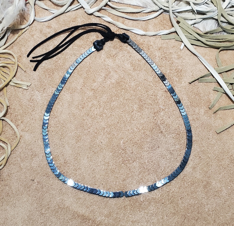 Pu&ograve; includere: Una collana d'argento con una catena fatta di piccoli pezzi metallici appuntiti. La collana ha un cordoncino in pelle nera con un fiocco.