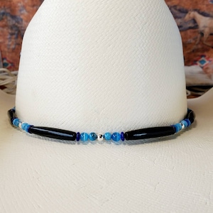 May include: A white cowboy hat with a blue and black beaded hat band. The hat band features black onyx, blue agate, and silver beads.