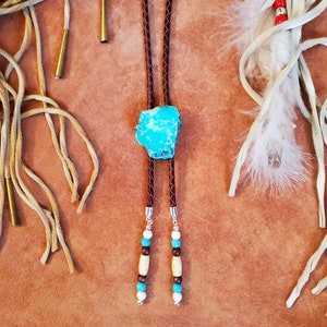 May include: A brown leather bolo tie with a turquoise stone and wooden beads. The tie is on a brown background.