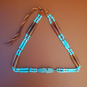 May include: A turquoise and brown beaded necklace with a leather tassel and a turquoise feather charm.