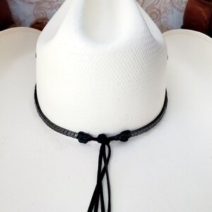 Pu&ograve; includere: Cappello da cowboy bianco con una fascia in pelle intrecciata nera e un cinturino per il mento in pelle nera.
