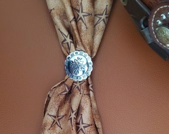 May include: A silver bolo tie with a star-shaped design. The tie is tied around a brown bandana with a white star pattern.
