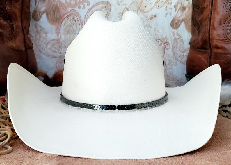 Pu&ograve; includere: Un cappello da cowboy bianco con una fascia nera a forma di chevron.
