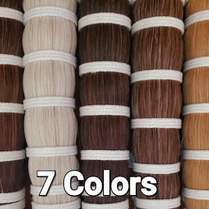 Puede incluir: Siete paquetes de extensiones de cabello en varios tonos de marrón, rubio y negro, cada uno envuelto con una cuerda blanca. El texto "7 Colors" se muestra en la parte inferior de la imagen.