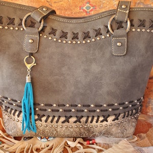 May include: A gray faux leather tote bag with black stitching and silver studs. The bag has a turquoise tassel attached to a silver key chain.