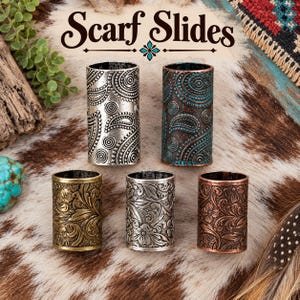 May include: Five cylindrical scarf slides arranged in two rows. The top two feature a paisley pattern in silver and a dark copper with teal accents. The bottom three display floral engravings in antique gold, silver, and copper finishes.